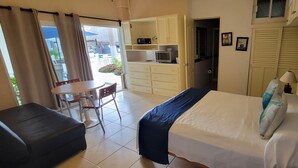 Een slaapkamer met een bed, een klein tafeltje en een kitchenette.