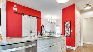 Eine Küche mit roter Akzentwand, einem Edelstahl-Geschirrspüler und einer Spüle im Bauernhausstil.