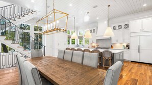 Une cuisine moderne avec des meubles blancs, une table à manger en bois et un escalier doté de rampes noires.