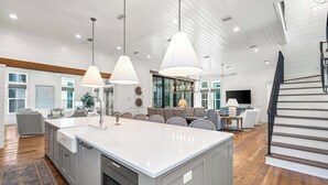 Une cuisine spacieuse avec un grand îlot central, un plancher en bois et des luminaires suspendus.