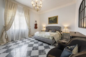 A bedroom with a checkered floor, a bed with a grey upholstered headboard, a violin, and a painting on the wall.