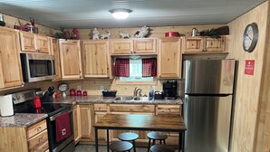 A kitchen with wooden cabinets, stainless steel appliances, a red and black checkered towel, and a clock on the wall.