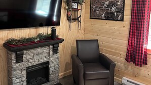 A cozy living room with a stone fireplace, a mounted TV, a framed wildlife photograph, and a plaid curtain.