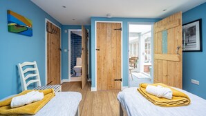 Une chambre avec deux lits, une porte en bois, un mur bleu et une lucarne.