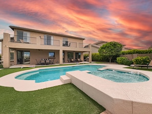 A two-story house with a swimming pool, outdoor furniture, and a well-maintained lawn.