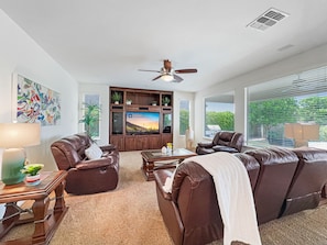 A living room with a large flat-screen TV, leather sofas, a coffee table, and a ceiling fan.