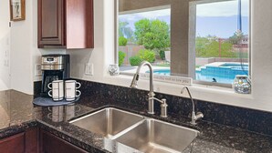 Una cocina con un lavamanos doble, una cafetera y vistas a una piscina.