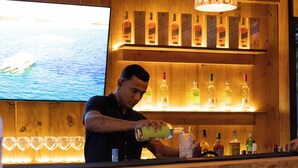 A bar area with wooden shelves displaying bottles, a bartender preparing a drink, and a sign reading "LOUNGE & BAR LUNA HOTEL BOUTIQUE". - LUNA Hotel Boutique (Guarujá)