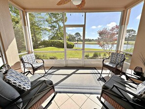 A sunroom with large windows, wicker furniture, and a view of a lake and trees.