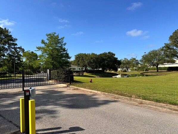 A gated entrance to a park with a grassy area and a pond.