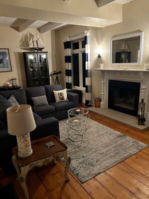 A living room with a dark sofa, a round coffee table, a lamp, a fireplace, and a striped curtain.
