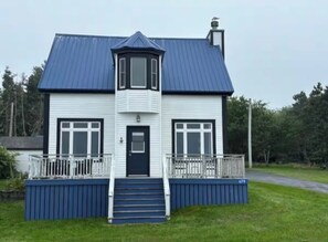 A two-story house with a blue roof, a central tower, and a front porch with steps. - Oceanfront 3-Bedroom Captain's House (Rose Bay)