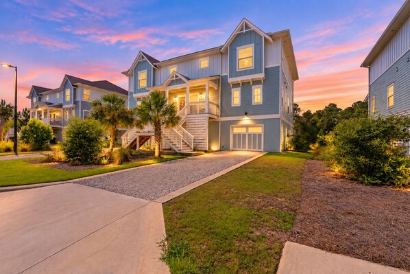 A two-story residential building with a front porch, a staircase, and a driveway.