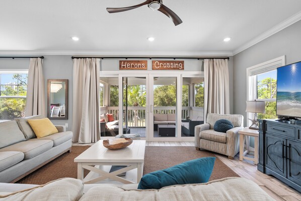 A spacious living area with a sofa, a coffee table, and a TV stand. There is a sliding glass door leading to an outdoor patio. - Heron's Crossing at Lost Key Golf & Beach Club | BIG Dog-Friendly | Beach Getaways (Pensacola)