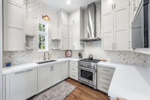 A modern kitchen with white cabinets, a stainless steel stove, and a window with a view of greenery. - Wave Jumper | Cottage in Rosemary Beach with Access to Rosemary Beach, Pools, Tennis, and Gym (Rosemary Beach)