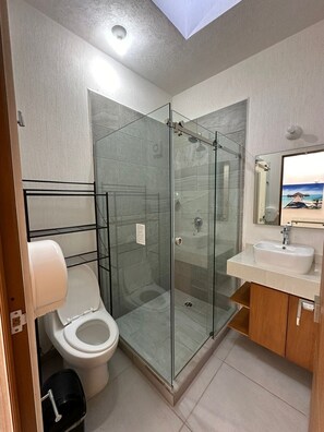 A modern bathroom with a glass-enclosed shower, a toilet, a sink, and a mirror. - Puerto Vallarta Altavela Capri 6 (Valle de Banderas)