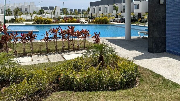 A modern hotel with a swimming pool, surrounded by greenery and palm trees.