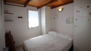 Une chambre avec un plafond en bois, un lit, une fenêtre et un mur décoré d’étoiles et de motifs.