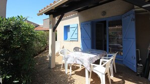 Une terrasse avec une table et des chaises, une porte bleue et une fenêtre avec des volets.