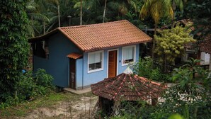 Una piccola casa a un piano con tetto in tegole, circondata da fitta vegetazione tropicale.