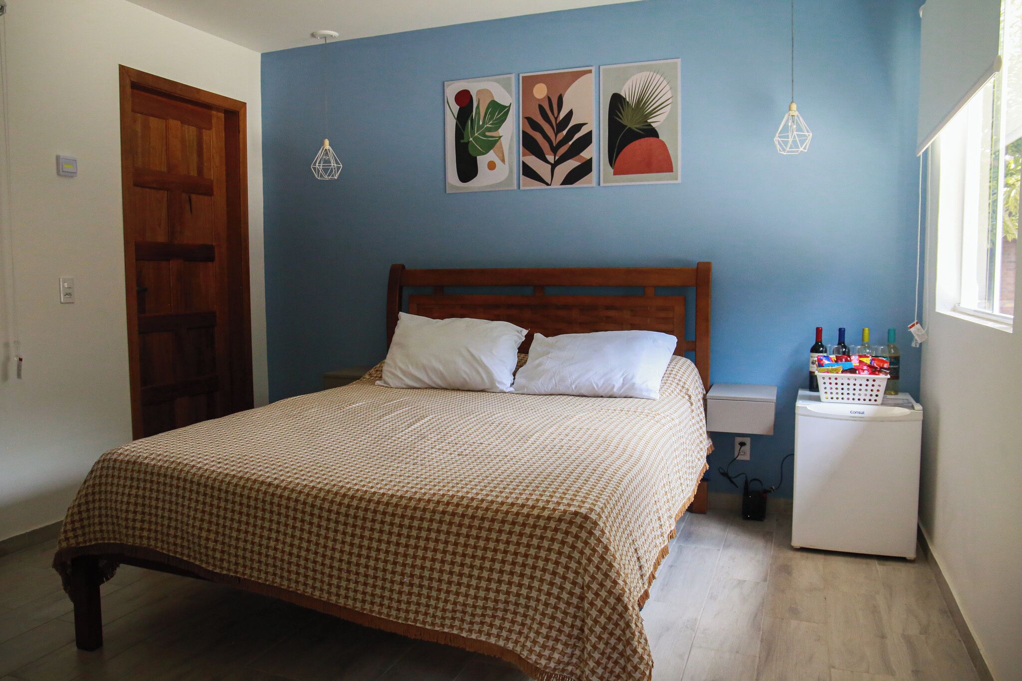 A bedroom with a wooden bed, a small bedside table, a wall-mounted light, and a window.