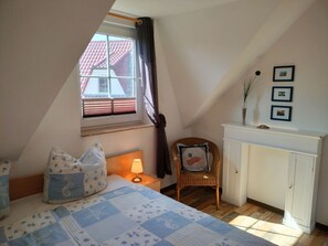 Una camera da letto con un letto, una sedia, un comodino, una lampada, una finestra con tende e un caminetto, con quadri appesi alle pareti.
