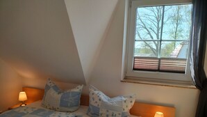 Un dormitorio con cama, dos lámparas de noche, una ventana con persianas y vistas a árboles y un edificio.