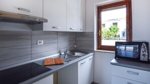 A compact kitchen with white cabinets, a built-in microwave, and a window with a view of a building and trees.