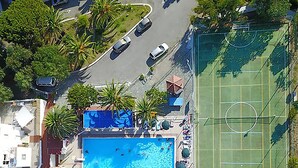 An aerial view of a residential area with a swimming pool, tennis court, and parked cars.