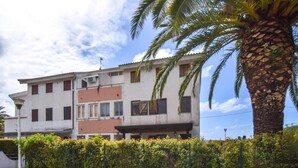A multi-story building with a mix of residential and commercial spaces, a palm tree, and a hedge in the foreground.