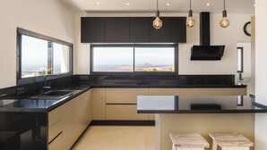 A modern kitchen with a large window, black cabinets, and pendant lighting. - CAPRICA by Buenavilla| Indulge in Serene Opulence at Las Breñas, Lanzarote. (Las Breñas)