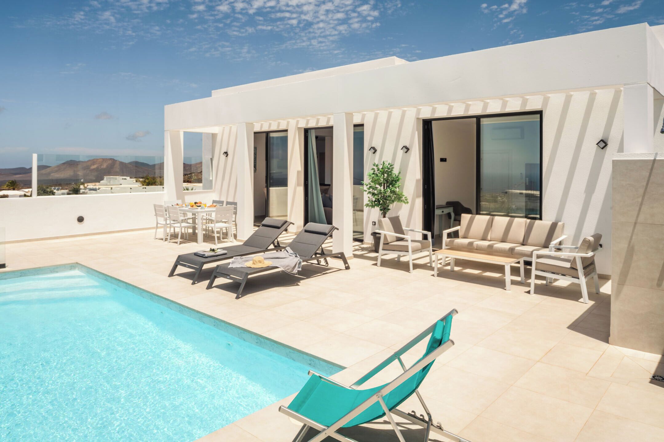 Un espace piscine extérieur moderne, doté de chaises longues, d’une table à manger et d’un canapé.