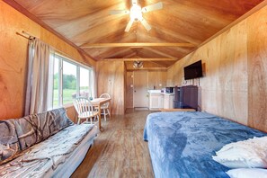 Una habitación acogedora con cama, sofá, mesa de comedor con sillas, zona de cocina y televisor en la pared.