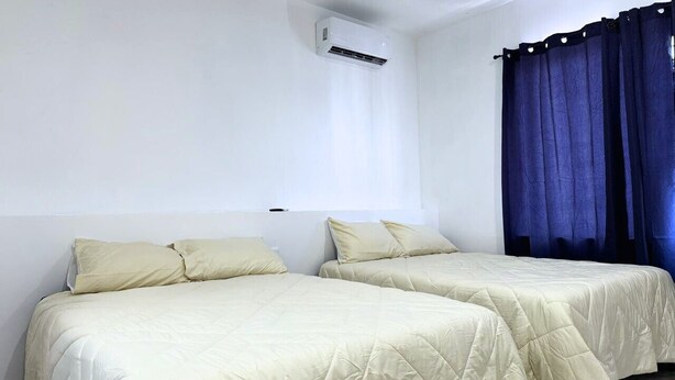 Une chambre avec deux lits, une fenêtre avec des rideaux et un appareil de climatisation.