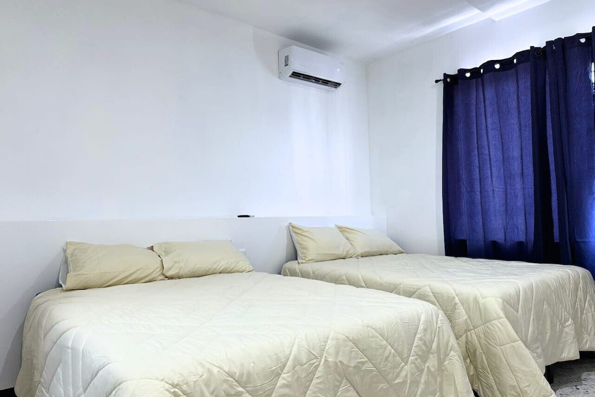 A room with two beds, a window with curtains, and an air conditioning unit.