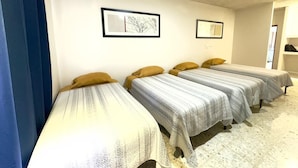 Une pièce avec quatre lits simples alignés contre un mur, chacun étant recouvert d’une courtepointe à motifs et agrémenté d’un oreiller. Deux tableaux encadrés sont accrochés au mur, au-dessus des lits.