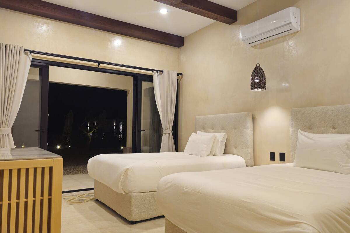 A hotel room with two beds, a desk, and a large window with curtains.