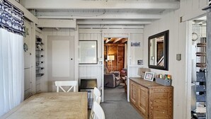 Een knus ingerichte kamer met een houten tafel, witte stoelen, een kleine televisie en een houten kastje met spiegel.