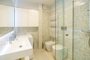 Un baño moderno con ducha envuelta en vidrio, lavamanos blanco y un bidé.
