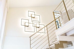 Un escalier orné d’un luminaire aux motifs géométriques fixé au mur et doté d’une rampe en métal.