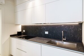 A modern kitchen with white cabinets, a black marble backsplash, and stainless steel appliances.