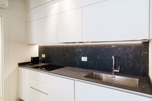 Uma cozinha moderna com armários brancos, painel de vidro preto marmorizado e eletrodomésticos de aço inoxidável.