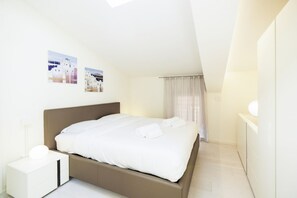 A bedroom with a bed, a bedside table, a nightstand, a window with curtains, and two wall-mounted pictures.