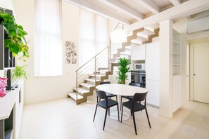 Una cocina moderna con armarios blancos, una mesa de comedor con sillas, una escalera y una planta en maceta.