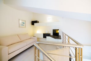 Una sala de estar moderna con un sofá, un televisor de pantalla plana y una escalera con barandilla de metal.