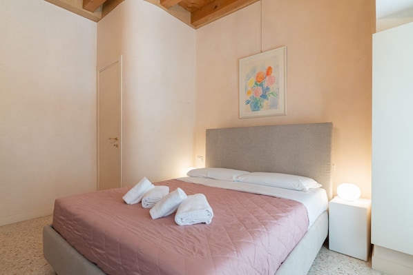 A bedroom with a bed, a bedside table with a lamp, a door, and a painting on the wall. - Fabulous residence overlooking Piazza Erbe (Verona)