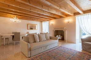 A cozy living room with a sofa, a dining table, chairs, a chandelier, a fireplace, and a patterned rug. - Fabulous residence overlooking Piazza Erbe (Verona)