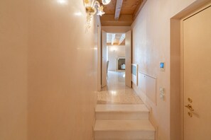 A hallway with a staircase leading to a door, a light fixture, and a thermostat on the wall.