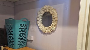 A room with a wooden dresser, a teal laundry basket, and a wall-mounted mirror with a seashell design.