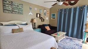 A bedroom with a large bed, a ceiling fan, a desk, a chair, a rug, and a wall with various decorations.